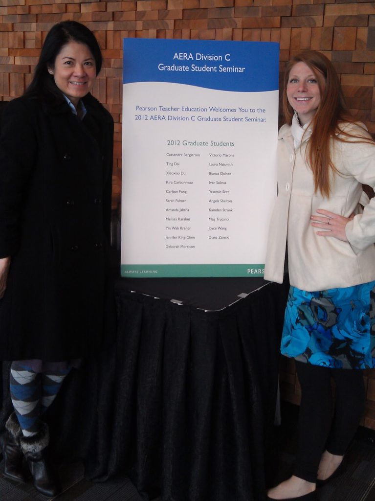 2 graduate ladies standing beside a chart at a conference session